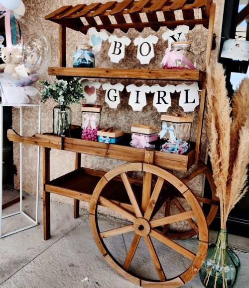 Candy bar installé pour une gender reveal avec décorations et friandises sur un chariot en bois.